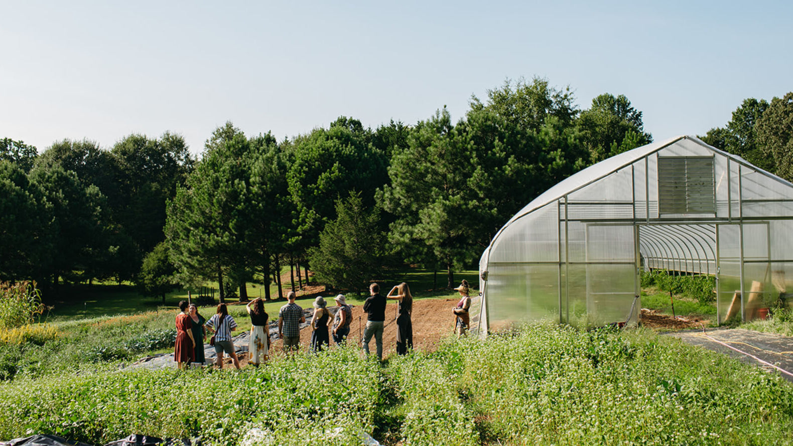 Group of people standing in a field with a greenhouse in the background