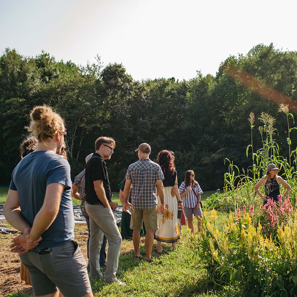 Group of people standing in a field with wildflowers and trees in the background
