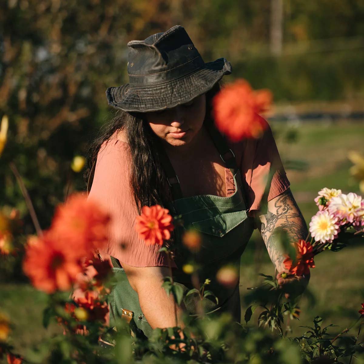 Person in a garden wearing a hat and apron, surrounded by flowers.