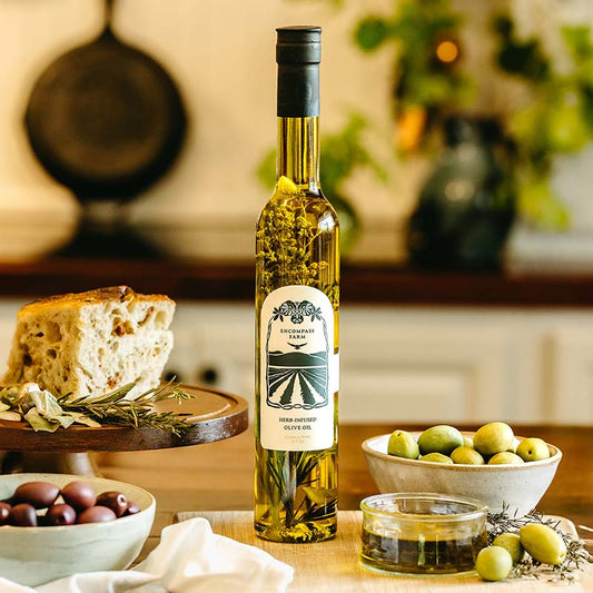 Bottle of infused olive oil from Encompass Farm on a table with bread and olives in a kitchen setting