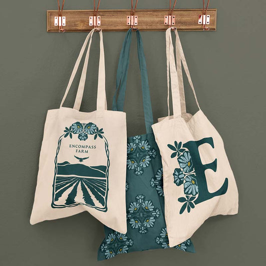 Encompass Farm tote bags hanging on wooden rack