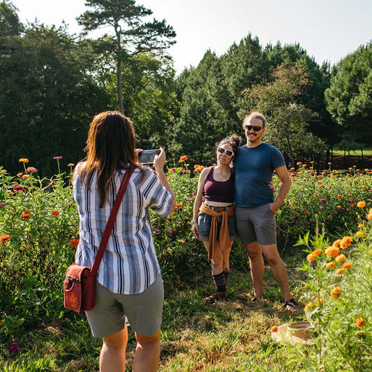 Two people taking a photo of another person in a field of flowers.